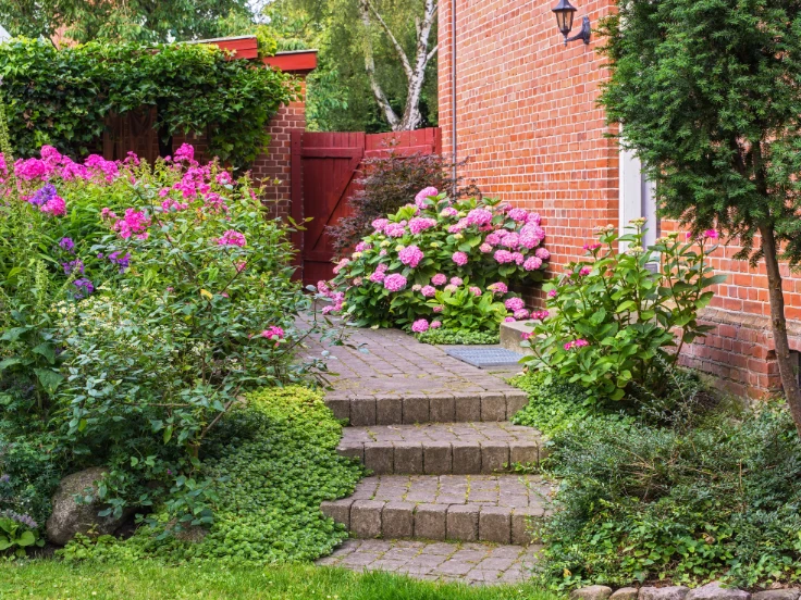 A serene garden featuring a brick wall and a winding path leading to a vibrant flower garden.