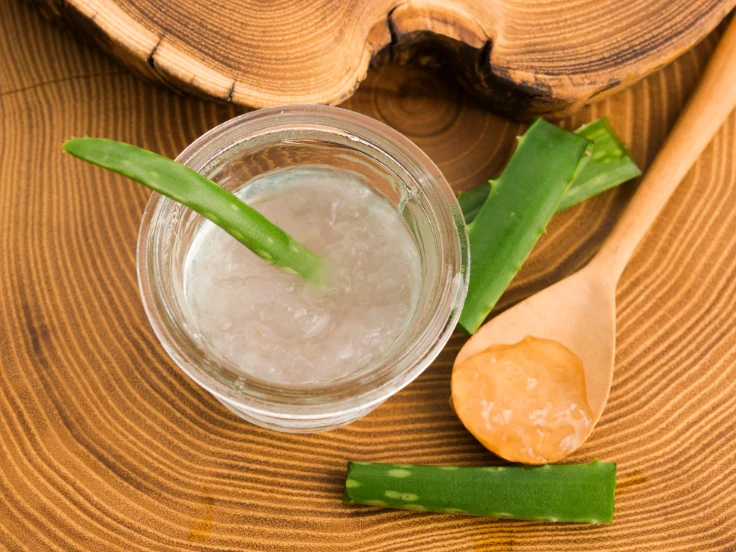Aloe vera gel in a glass jar with a wooden spoon, resting on a rustic wooden table.
