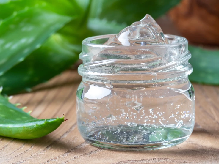 Aloe vera gel in a jar with a fresh leaf, placed on a rustic wooden table, showcasing natural skincare ingredients.