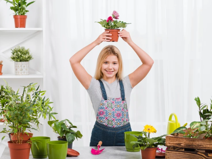 A girl joyfully holds a flower pot filled with vibrant green plants.