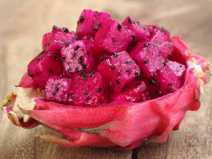 A halved dragon fruit showcases its unique texture and color, placed on a warm wooden table background.