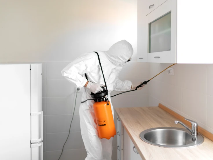 A man dressed in a white suit is spraying a kitchen, likely for maintenance or renovation purposes.