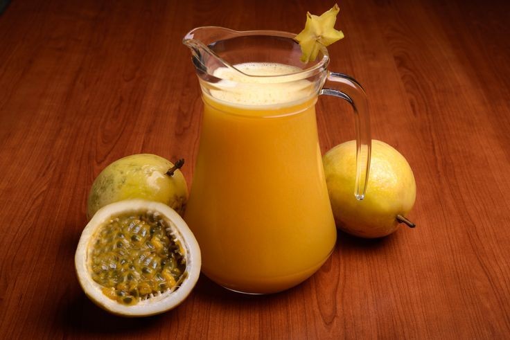 Glass pitcher of passion fruit juice with fresh fruit on wood table.