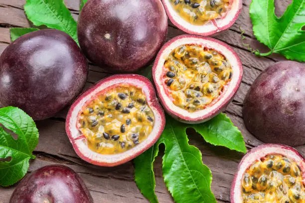 Sliced passion fruit with leaves on a wooden surface.