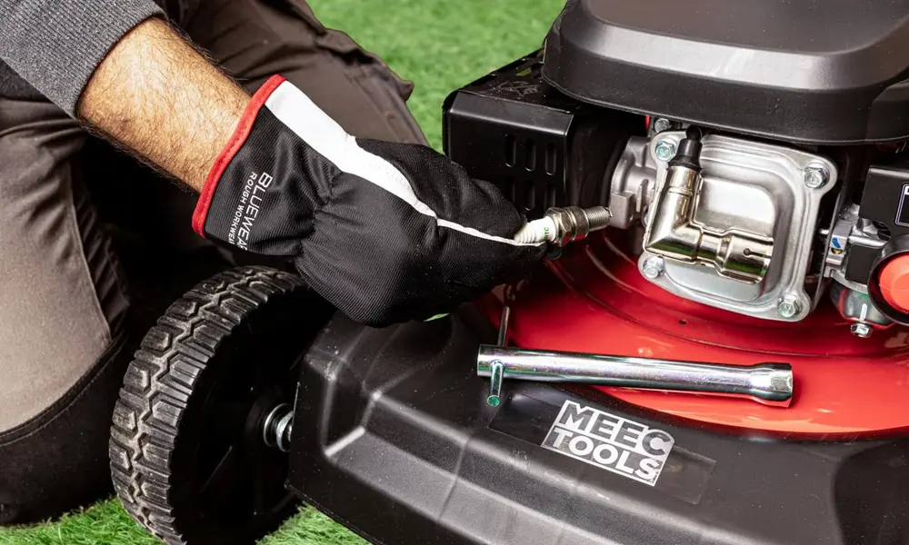 Peeacelily | Lawn Mower Repair: Common Problems and How to Fix Them A person wearing a work glove inspecting and replacing a spark plug on a lawn mower.