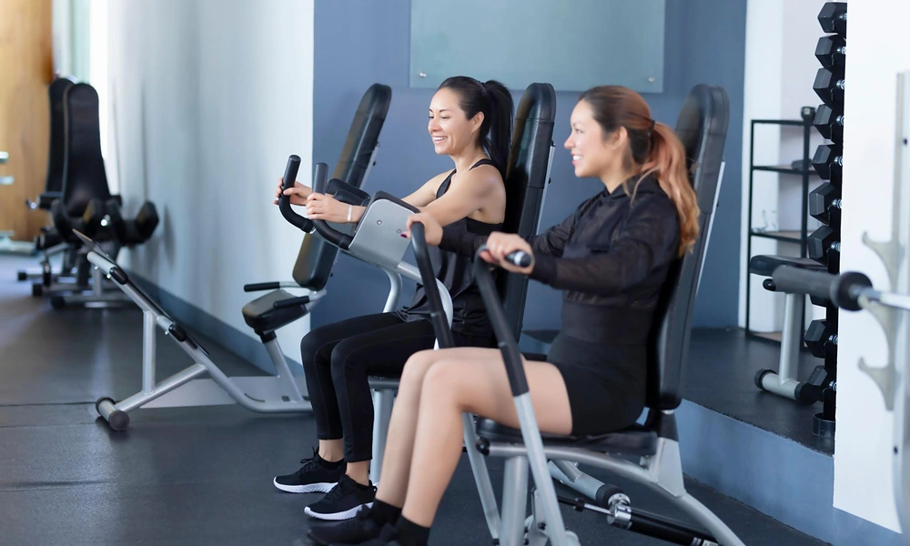 Peeacelily | Planet Fitness: Membership Costs, Equipment, Benefits, and What to Know Two women smiling while exercising on strength machines using a classic gym membership