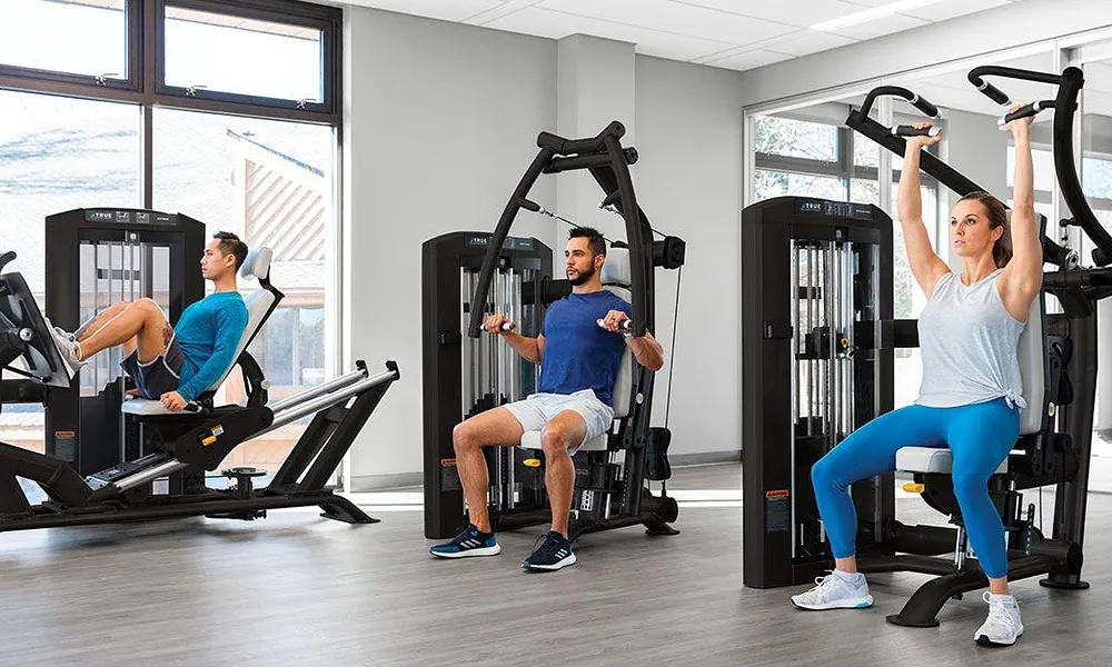 Peeacelily | Planet Fitness: Membership Costs, Equipment, Benefits, and What to Know Gym members exercising on guided selectorized strength machines in a bright workout area